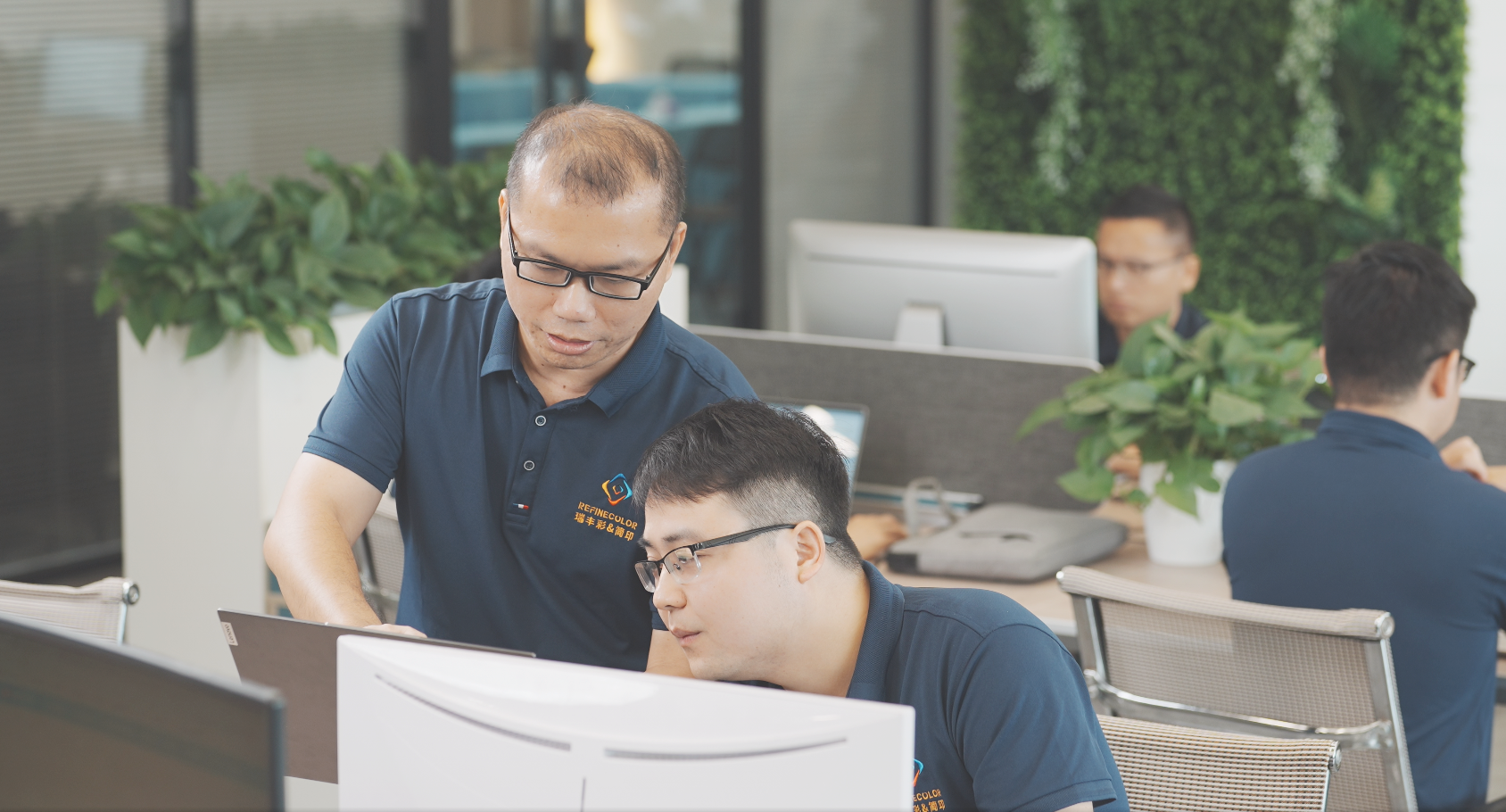 In this image, a team of professionals is working together in a modern office environment, exchanging ideas and providing technical guidance. The collaborative setting highlights the behind-the-scenes efforts in research, design, and customer support that contribute to the success of UV print machine technology. Surrounded by greenery and a well-organized workspace, the scene emphasizes innovation, teamwork, and dedication to advancing high-quality ultraviolet printing solutions.